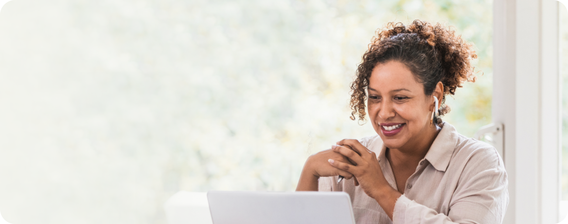 Woman wearing wireless earbuds smiling while looking at a laptop