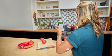 Woman checking her blood glucose on her smartphone as she chopping vegetables