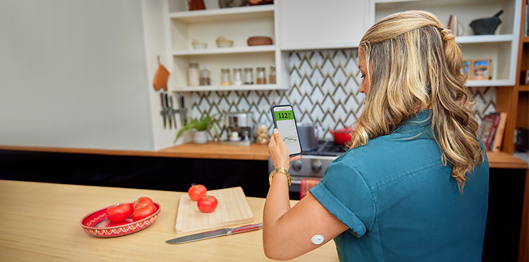 Woman checking her blood glucose on her smartphone as she chopping vegetables