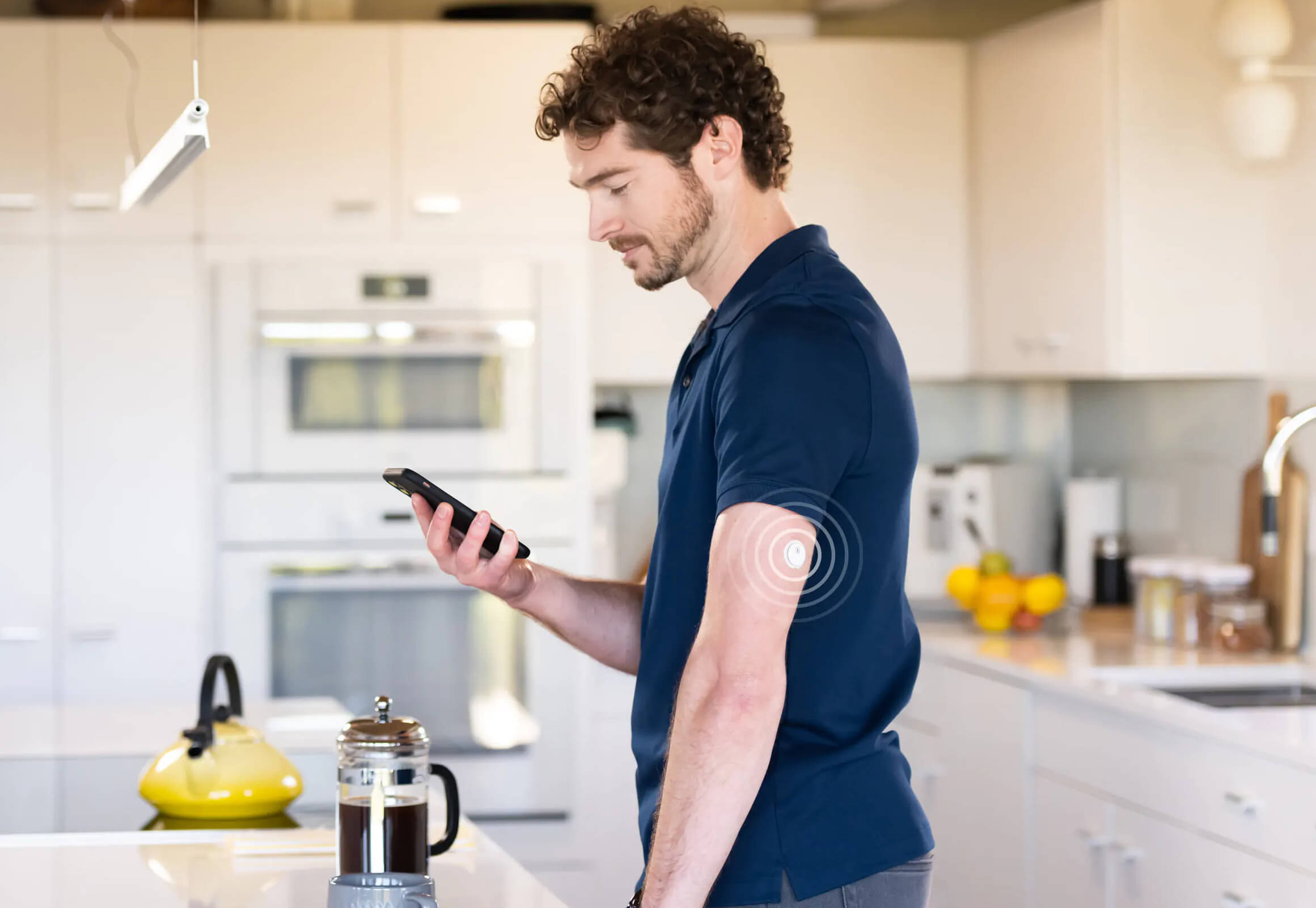 Mann mit FreeStyle Libre 3 Sensor am Arm steht in der Küche und schaut auf sein Handy