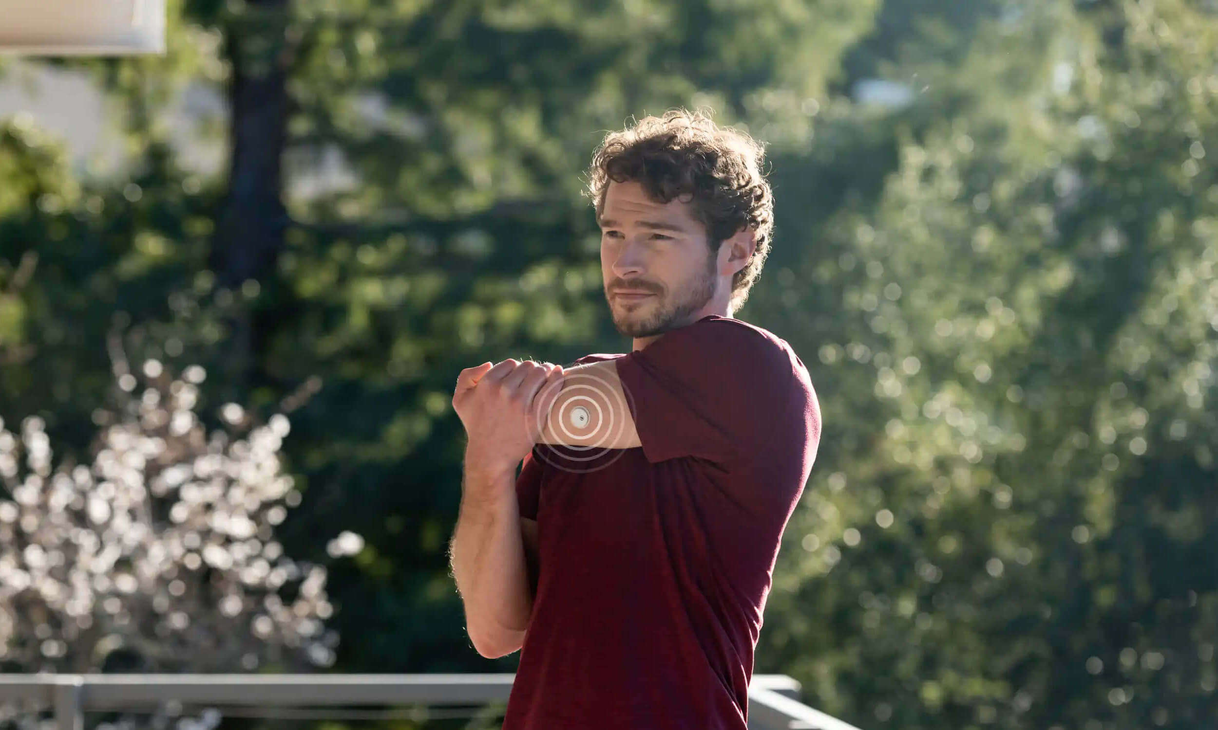 Mann mit FreeStyle Libre 3 Sensor am Arm steht in der Natur beim Stretching