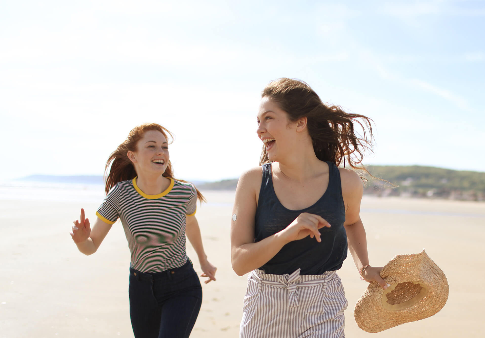 Zwei junge Frauen rennen am Strand und lachen.