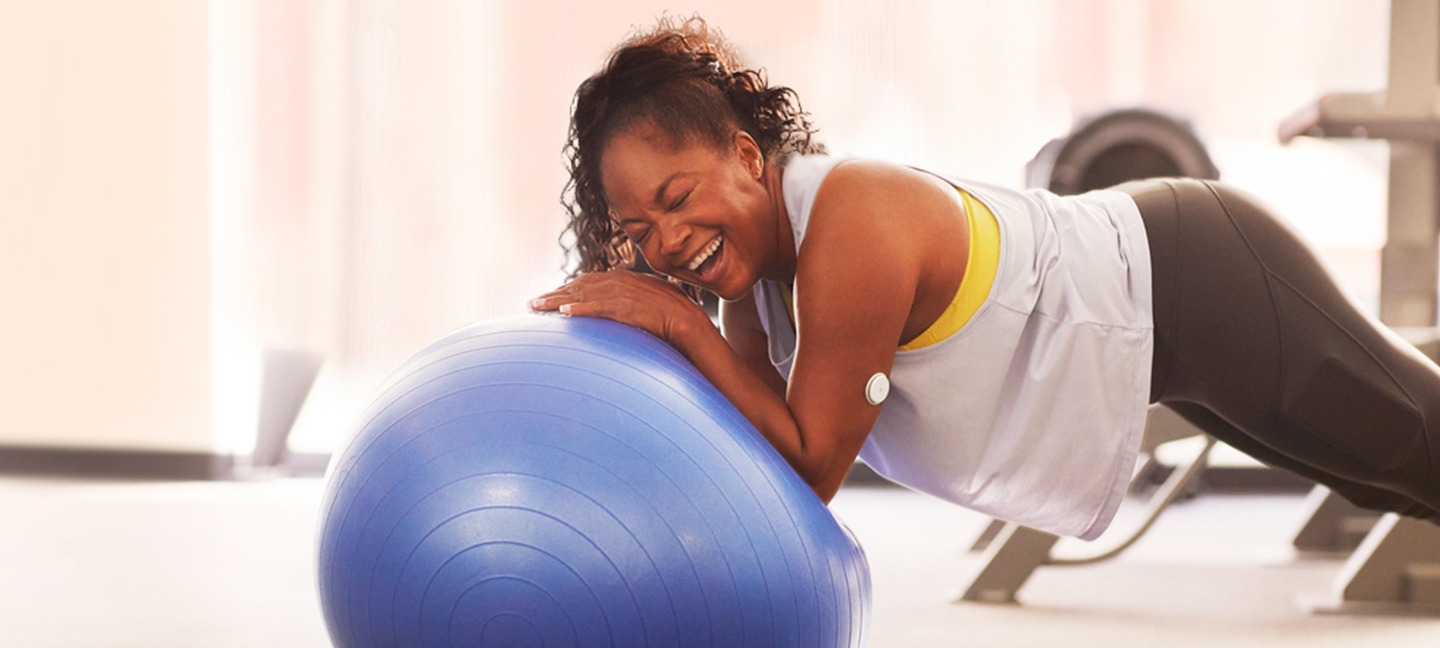 Woman with a FreeStyle Libre sensor on her arm smiling while balancing on a gym ball