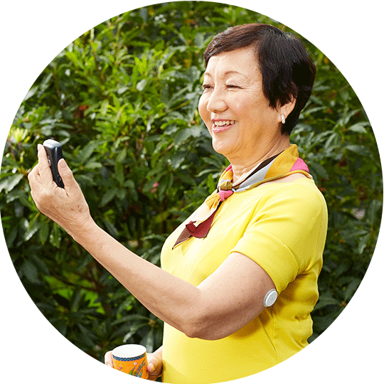 A smiling woman wearing a FreeStyle Libre sensor looking at her FreeStyle Libre reader