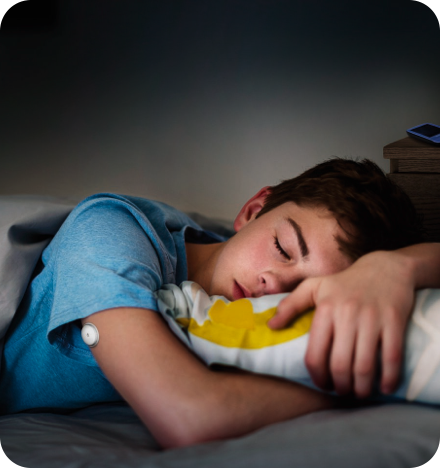 A boy sleeping in his bed with his sensor visible on his arm.