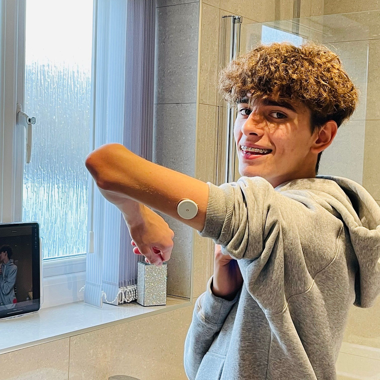 A boy looking at the camera smiling and showing his FreeStyle Libre sensor that is applied on the back of his arm.