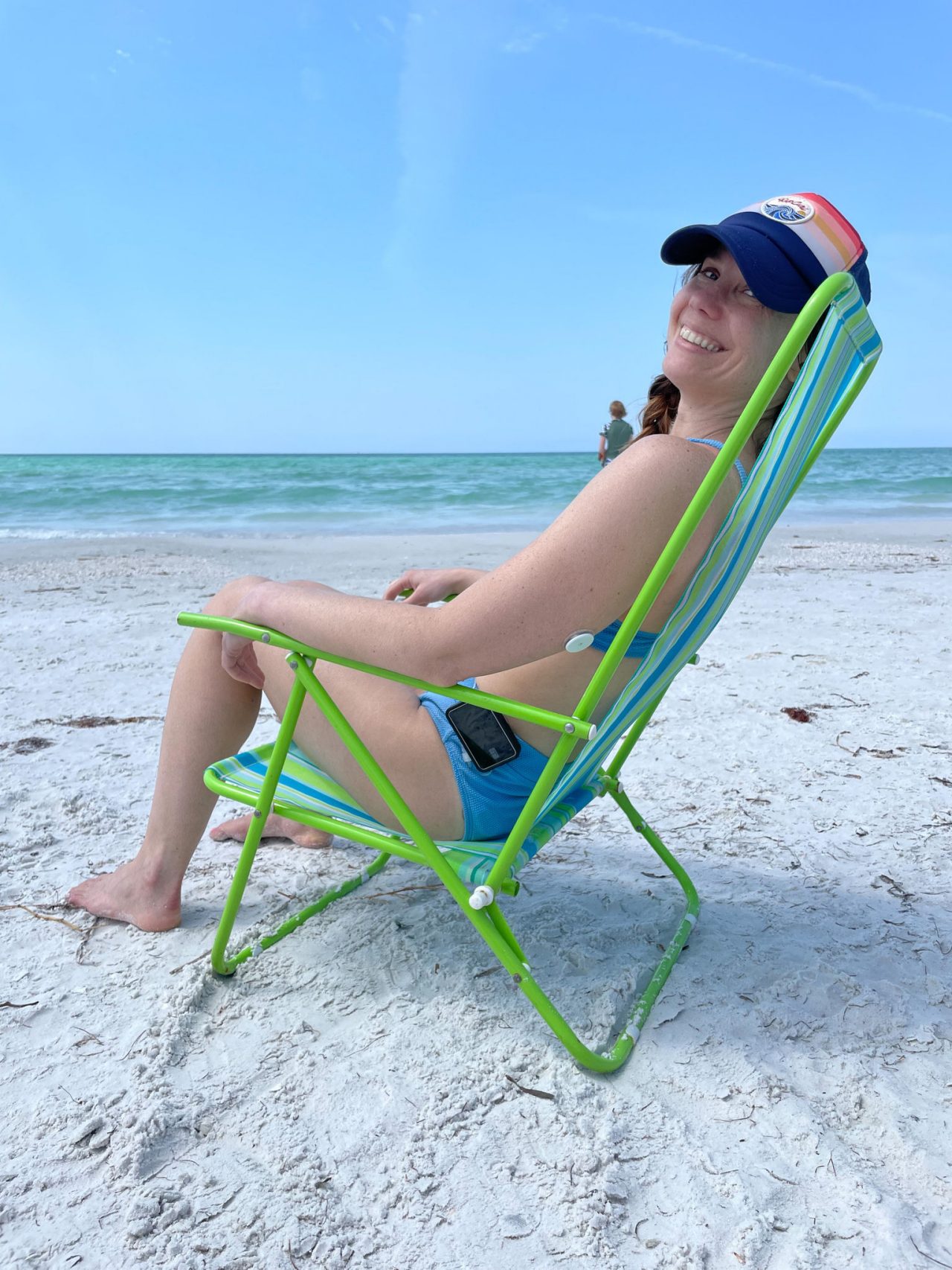 Erin, Blog author, sitting on a beach chair in front of the ocean smiling with FreeStyle Libre sensor visible on the back of her upper arm